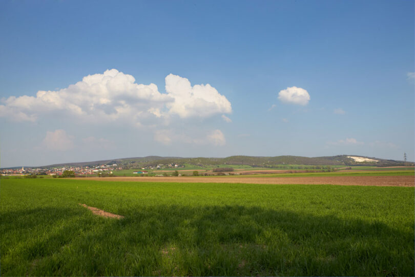 Weite Felder unter Wolkenhimmel, dahinter eine Ortschaft.