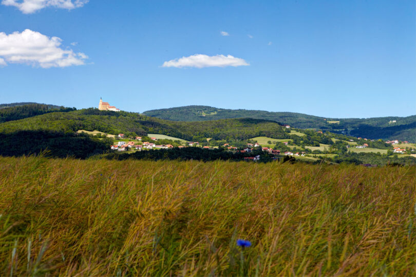 Weites Feld mit hügeliger Kulisse, im Hintergrund ein Schloss.