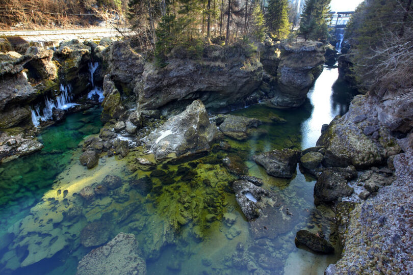 Flusslandschaft neben bewaldeter Straße. Felsreliefs mit fließendem Wasser und klarem Fluss.