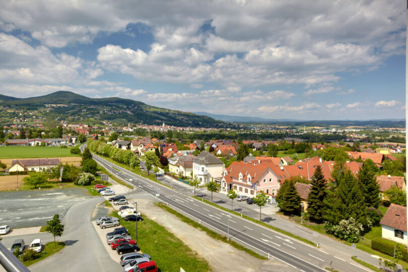 Städtische Bebauung entlang einer Straße, dahinter grüne Landschaft.
