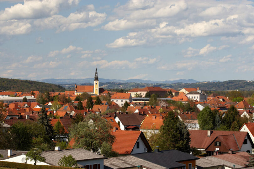 Dorflandschaft mit gelber Kircher im Zentrum. Eingebettet in sanfte Hügellandschaft.