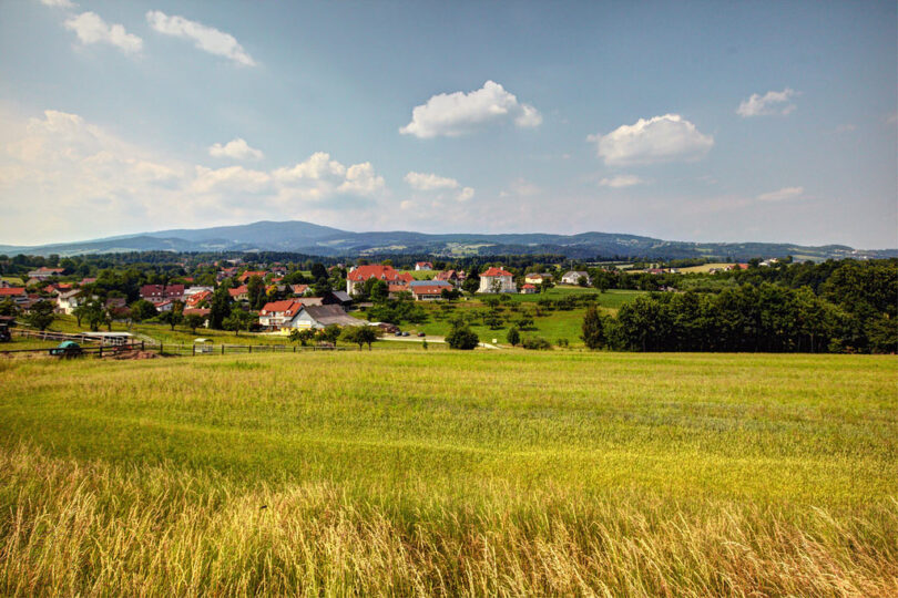 Offenes Feld, dahinter eine Ortschaft und angrenzender Wald.