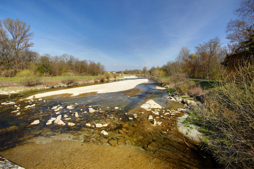 Flusslauf mit begleitenden Wegen und Bäumen entlang des Ufers.