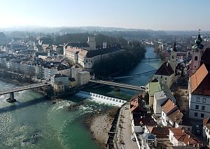 Luftaufnahme einer Altstadt mit Fluss, Wehranlage, mehreren Brücken und historischen Gebäuden im Morgendunst.