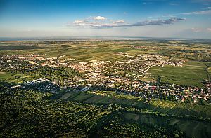 Weitwinkelaufnahme einer kleinen Stadt inmitten von Feldern und Wäldern unter blauem Himmel mit Wolken.
