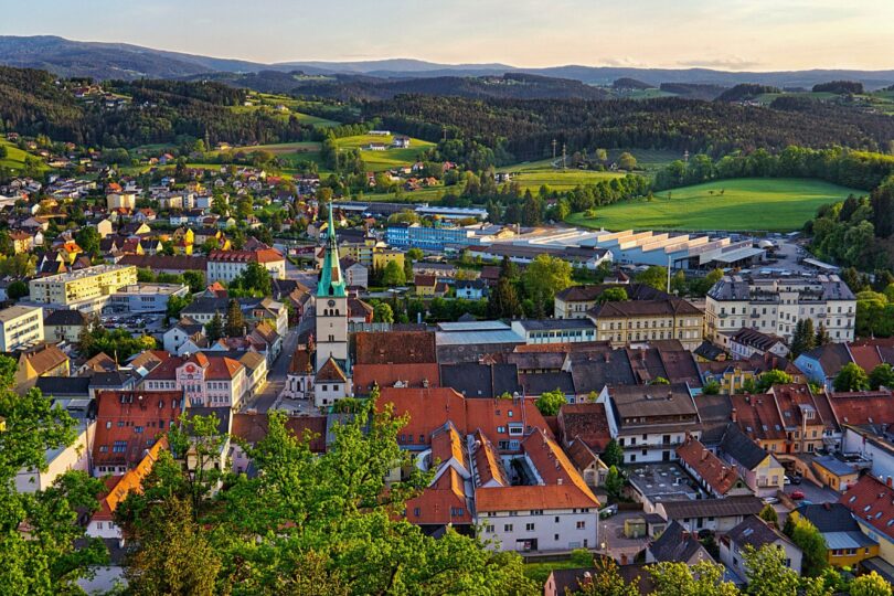 Luftaufnahme einer Kleinstadt mit Kirche, roten Dächern und umliegenden Hügeln im Abendlicht.