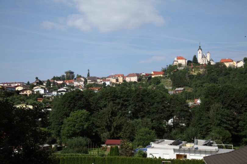 Kleines Dorfzentrum umgeben von viel Grün, mit einer Kirche als Mittelpunkt.