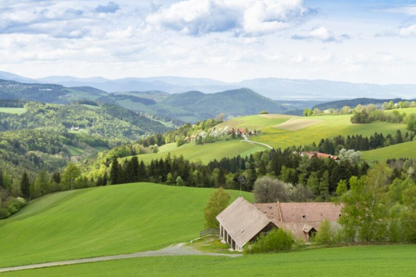 Weite Hügellandschaft mit grünen, offenen Wiesen und Bauernhöfen.