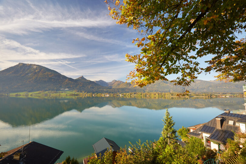 Berglandschaft vor See mit Reflexion der Berge im See. Am Rande sind Häuser am See sichtbar.