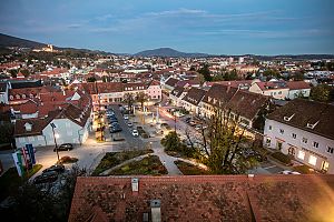 Stimmungsvolle Abendaufnahme einer Kleinstadt mit roten Dächern, beleuchteten Straßen und Hügelkulisse.