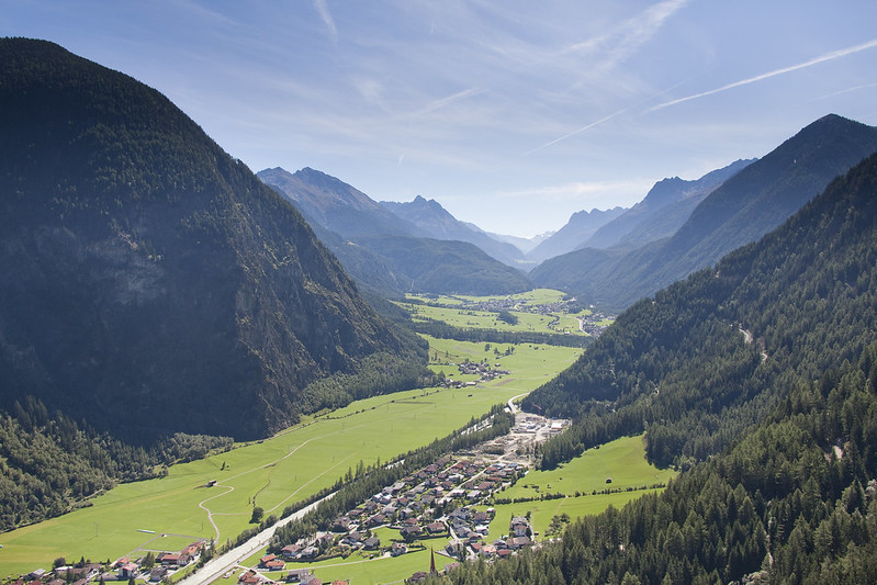 Dorf im Tal, eingerahmt von grünen Wiesen und umliegenden Bergen.