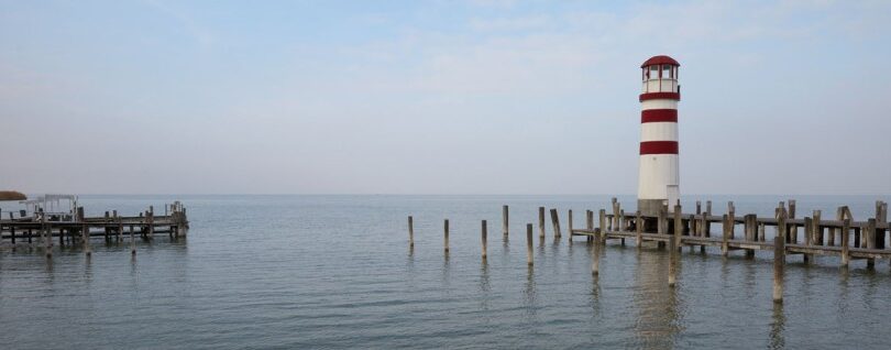 Leuchtturm am Ufer, daneben ein Steg ins Wasser.