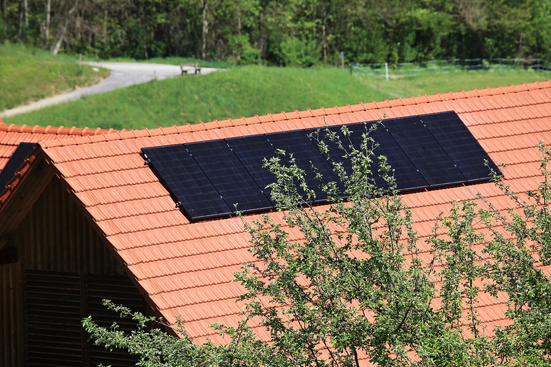 Hausdach mit Solarpanelen, angrenzend an Straße und offene Wiese.