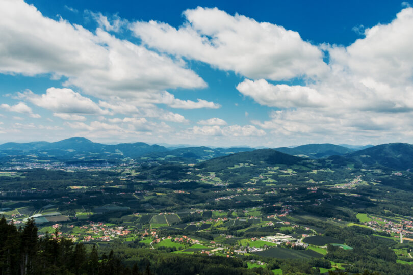 Weitblick über eine grüne Hügellandschaft mit verstreuten Dörfern unter blauem Himmel mit Wolken.