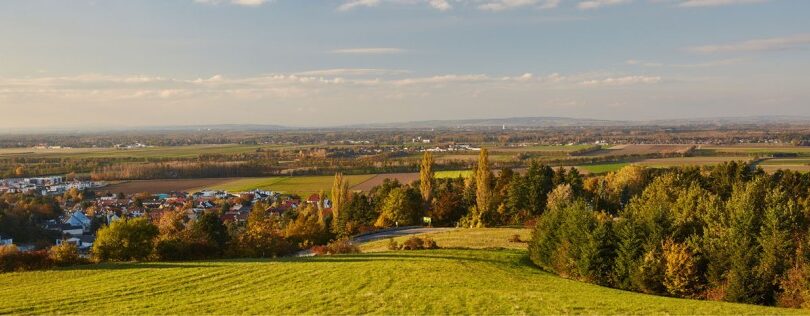 Landschaft mit Feldern und Bäumen, links davon ein Dorf.