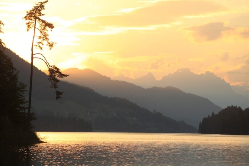 Stimmungsvoller See bei Sonnenauf- oder -untergang, umgeben von Bergen.