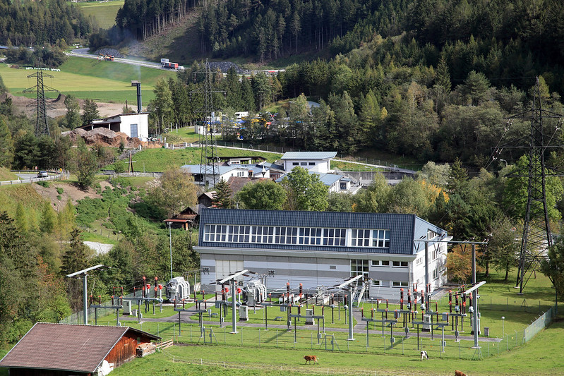 Elektrizitätswerk umgeben von Wald und Wiese. Im Hintergrund Industriegebiet.