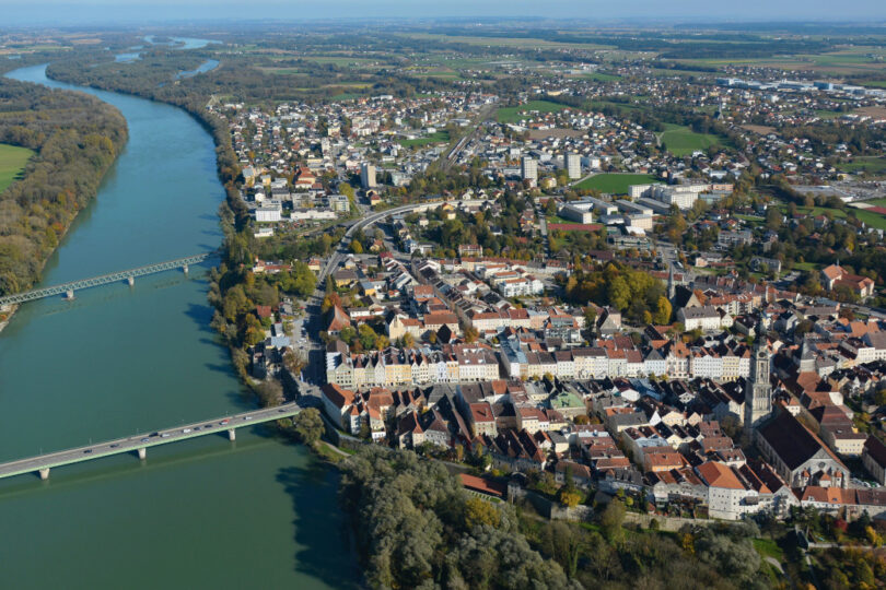 Luftaufnahme einer Stadt an einem Fluss mit Altstadt, Brücken, Wohngebieten und umliegender Landschaft.