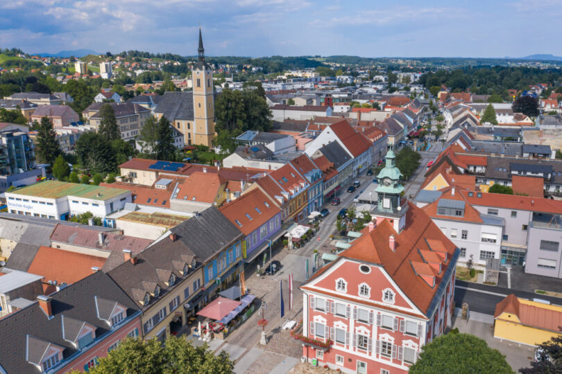 Luftaufnahme eines farbenfrohen Stadtzentrums mit Rathaus, Kirche, Altbauten und belebter Einkaufsstraße.