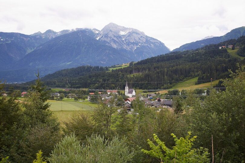 Dorfkirche und Dorf vor bergiger Kulisse.