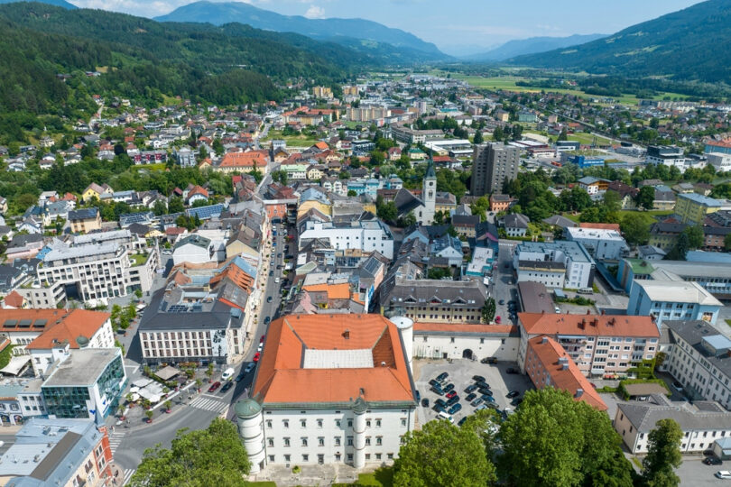Luftaufnahme einer Stadt im Alpenvorland mit Schloss, Kirchturm, Altstadtgasse und moderner Bebauung im Tal.
