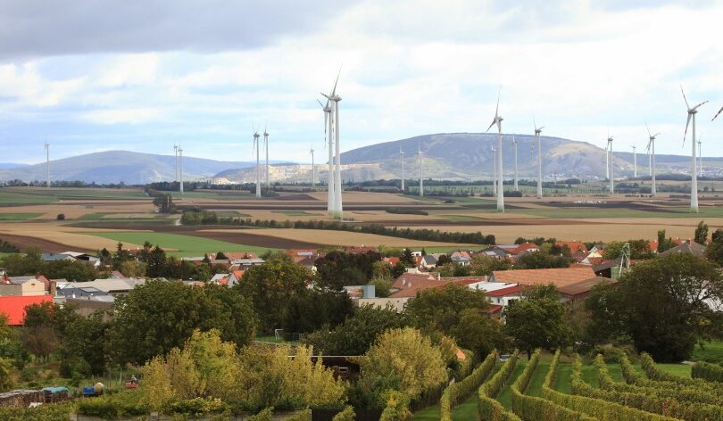 Landschaft mit Feldern und Dorf, dahinter Windräder.