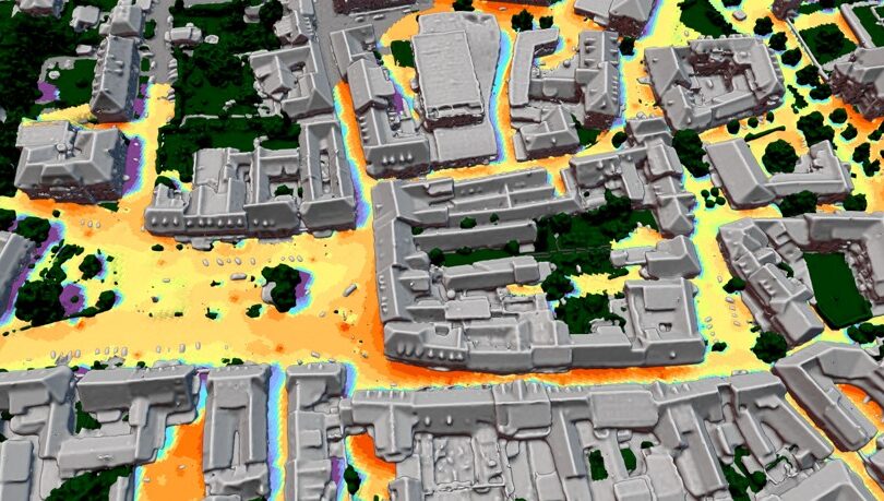 3D-Modell einer Stadt mit grauen Gebäuden, umgeben von grüner Vegetation und orangefarbenen Flächen, die die Wärmeverteilung darstellen.