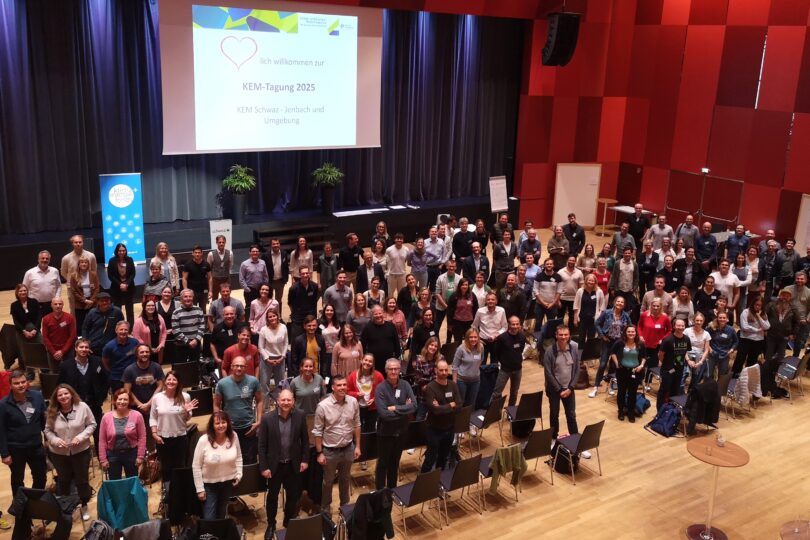 Gruppenfoto von etwa 150 Personen in einem Veranstaltungsraum. Die Teilnehmer stehen in Reihen, einige tragen Namensschilder. Im Hintergrund ein Banner mit 'KEM-Tagung 2025'.