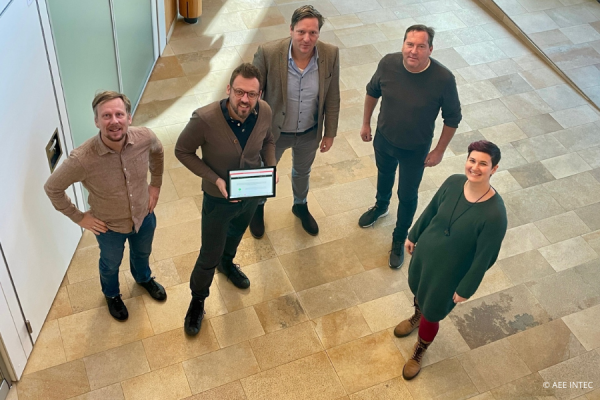 5 Personen stehen in einem Bürogebäude mit einem Tablet und werden von oben fotographiert.