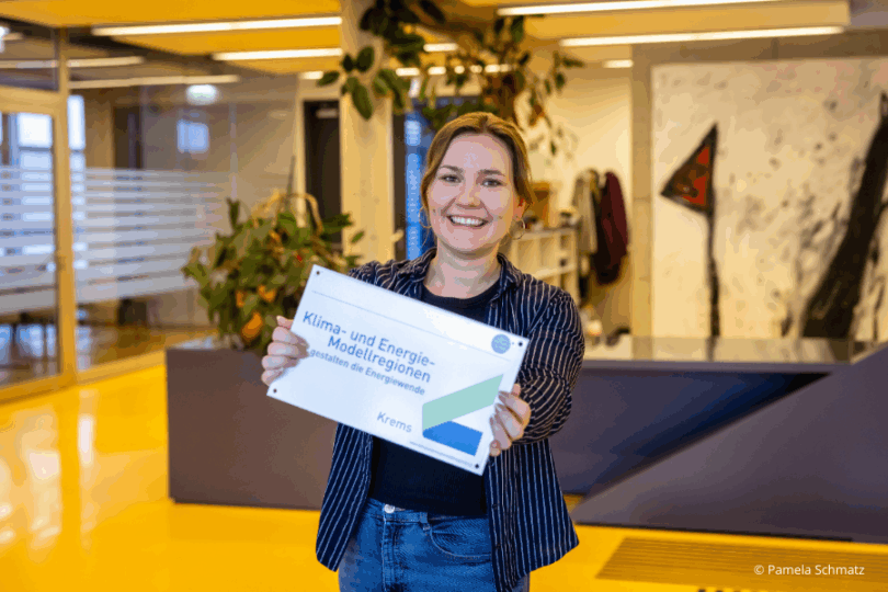 Frau mit KEM-Schild in den Händen in Bürogebäude.