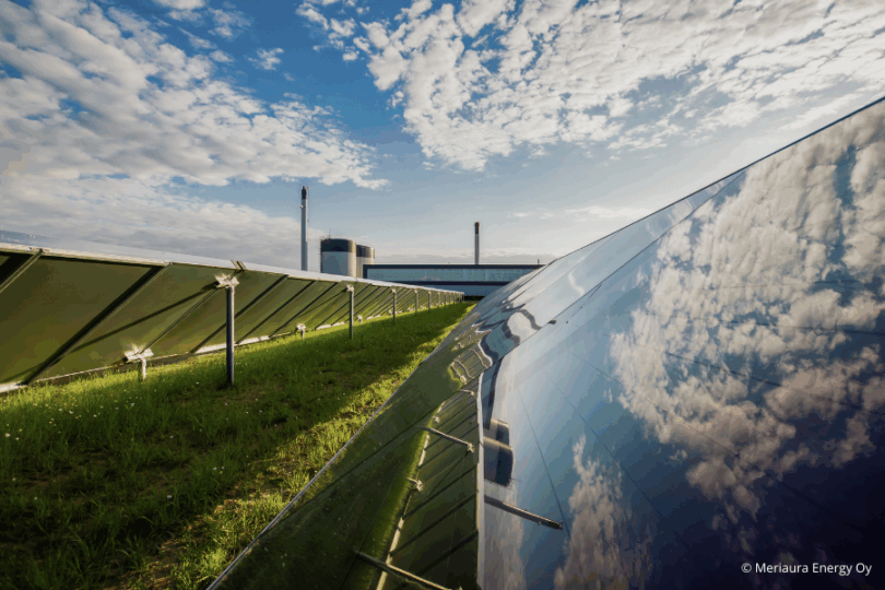 Freiflächen-PV-Anlage auf einer Weise, wo der Himmel mit Wolken reflektiert wird. Him Hintergrund Industriegebäude.
