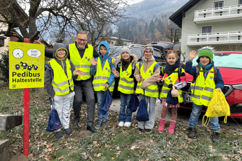 Kinder in Warnwesten draußen neben einem Warmschild.