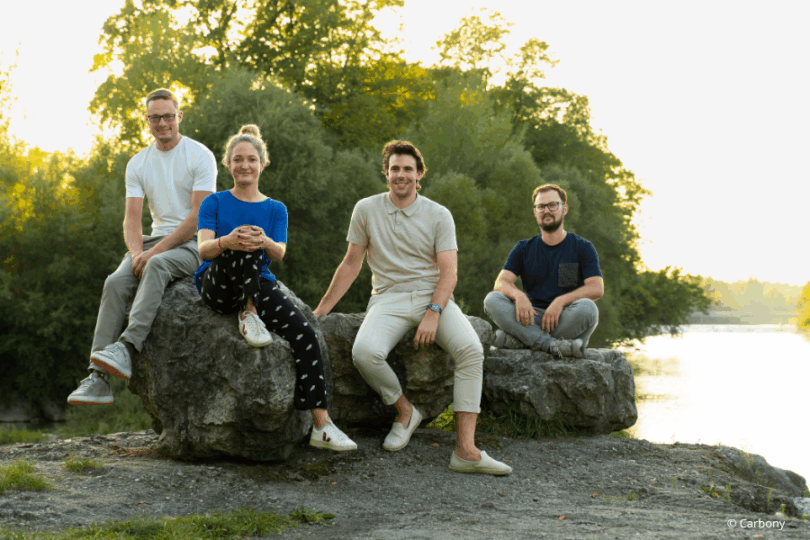 Vier Personen sitzen auf großen Steinen neben Fluss.