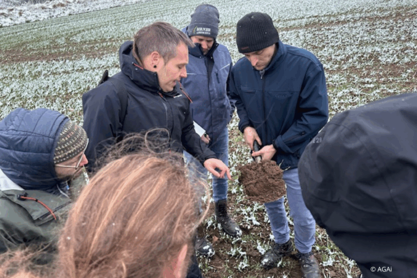 Menschen sehen eine Bodenprobe in einem winterlichen Feld an.