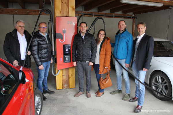 Sechs Personen stehen vor einer Ladestation für E-Autos, während zwei E-Autos geladen werden.