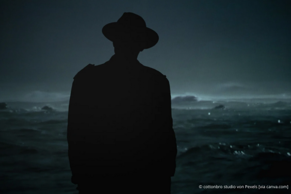 Umriss einer Person mit Hut vor einer dunklen Wiesenlandschaft bei Nacht.