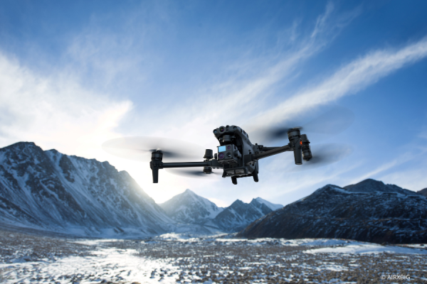 Drohne fliegt über Landschafft mit schneebedeckten Bergen im Hintergrund.