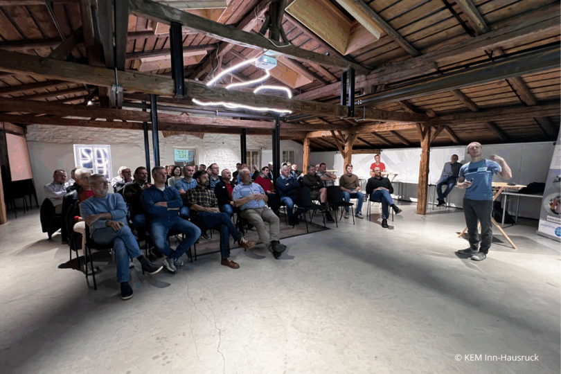 Menschen sitzen in Kinobestuhlung in einem Saal mit Holzdach.