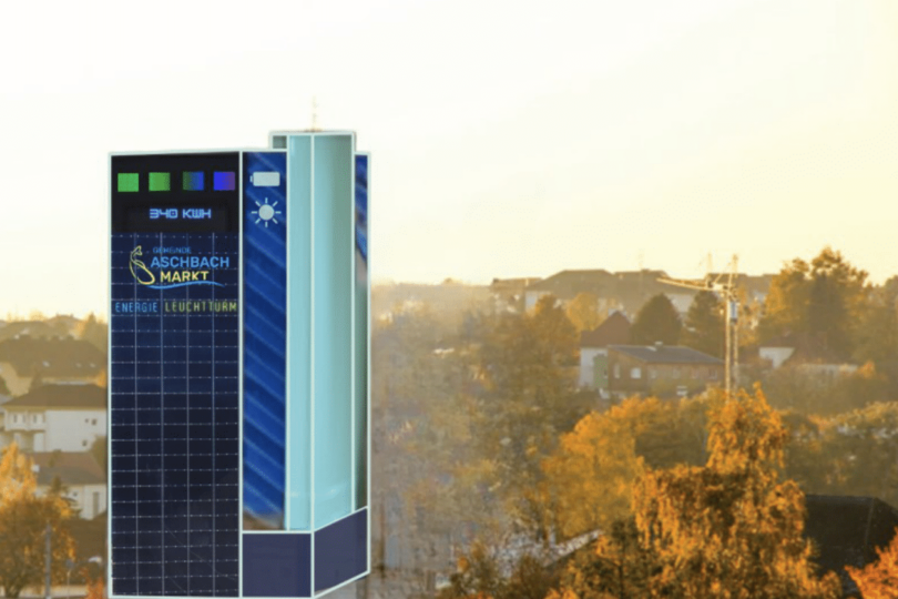 Ein mit Solarzellen verkleideter Turm mit digitalen Anzeigen über einem Stadtbild in der Abenddämmerung.