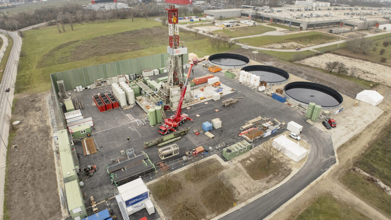 Man sieht einen Bohrturm, runde Wasserbecken und industrielles Gelände