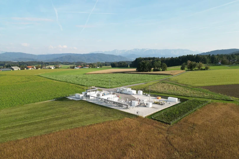 Luftaufnahme einer Industrieanlage mit mehreren weißen Tanks und Gebäuden, umgeben von landwirtschaftlichen Feldern und Bergen im Hintergrund.
